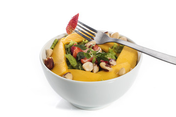 A healthy fresh salad of green lettuce with nuts, mango, strawberry, tomatoes in a white bowl isolated over white background.