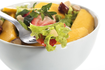 A healthy fresh salad of green lettuce with nuts, mango, strawberry, tomatoes in a white bowl isolated over white background.