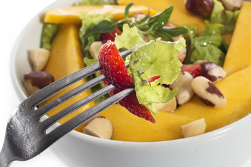 A healthy fresh salad of green lettuce with nuts, mango, strawberry, tomatoes in a white bowl isolated over white background.