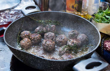 Frying homemade meatballs with rosemary on a ceramic covered frying pan