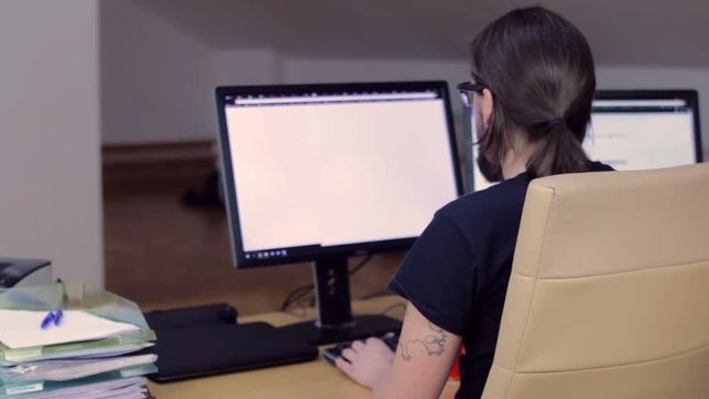 Bearded man working in office with 2 monitors