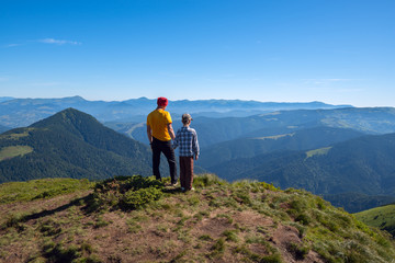 Fototapeta na wymiar Father and son stand on peak and look into the distance - wonderful adventure in outdoor. Sunny wonderful day in the mountains. Back view.