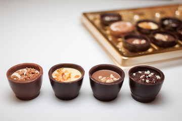Quattro dolci al cioccolato con ripieni diversi in primo piano. in background offuscata scatola d'oro di cioccolatini su uno sfondo bianco