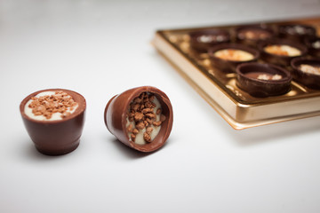 Due dolci al cioccolato con ripieni diversi in primo piano. in background offuscata scatola d'oro di cioccolatini su uno sfondo bianco