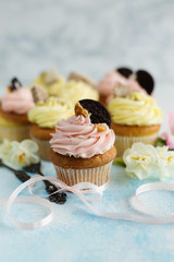 Delicious spring cupcakes with pink and yellow cream,decorated with cookies and waffles, on a light background (close-up)