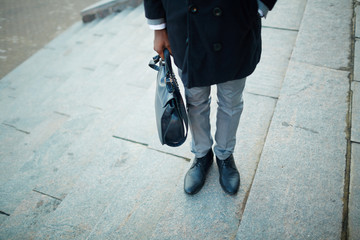 Low section portrait of one unrecognizable businessman standing on steps of office building wearing coat, shiny leather shoes and holding briefcase