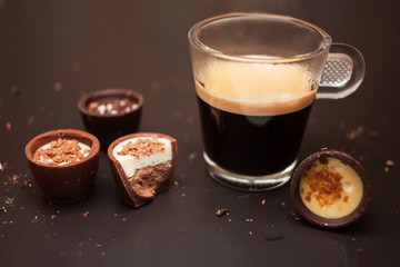 Una tazza di caffè nero con una varietà di cioccolatini su uno sfondo nero