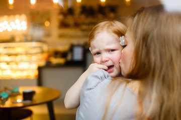 Girl in tears looking at camera while mother kissing her