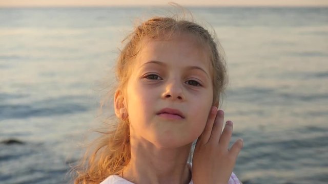 beautiful caucasian little girl on a background of sea sunset shows and inflate her lips