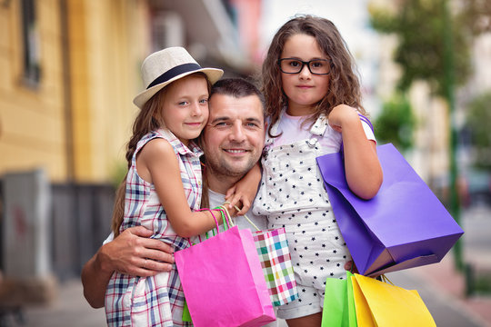 Happy daughters hugging father with shopping bags