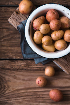 Raw potatoes in the metal bowl on the wooden table top view