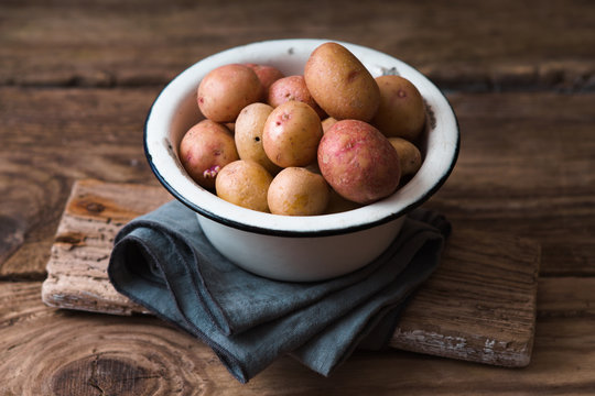 Raw potatoes in the metal bowl on the wooden table
