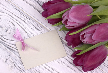 Purple tulips with white paper on a white wooden background with card for text. Womans Day. 8 March. Mother's Day.