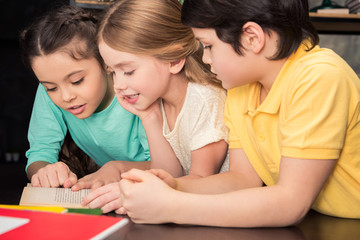 Three schoolchildren leaning at table and reading book together