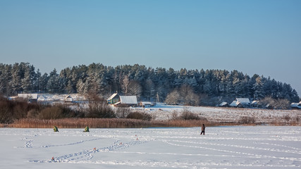 Evening on winter lake. Silhouettes of fishermen on ice background.