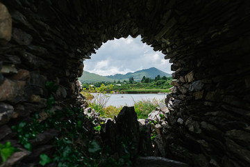 Blick durch Loch in Steinmauer auf grüne Berge