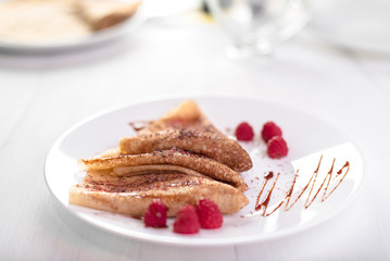 Three Russian thin pancakes and crepes folded triangle with raspberries, caramel sauce and chocolate chips on white plate