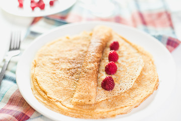 Russian thin pancake with raspberries on white plate, closeup