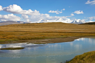 White wide river on a background of rocky hills under white clouds and blue sky, Plateau Ukok, Altai mountains, Siberia, Russia
