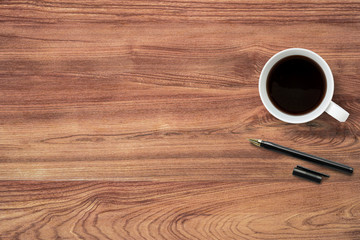 Cup of coffee and pen are on top of wood table. Top view with copy space, flat lay.
