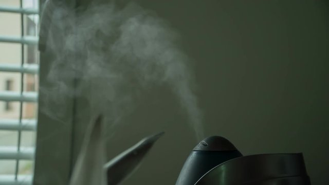 We can see a black tea maker which is standing on the kitchen counter and there is a lot of steam coming out of the device.
