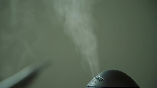There is a lot of steam coming out of a black tea maker which is standing on the counter in the kitchen.
