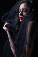 Gothic female face in a black veil looking down. Vertical studio shot.