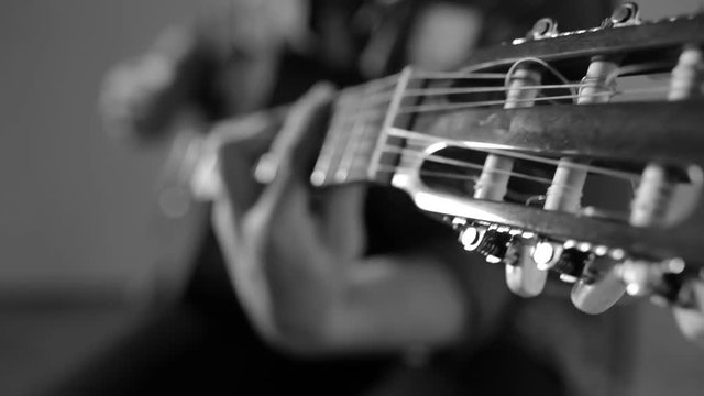 Closeup of guitarist playing on acoustic guitar sitting at gray wall background - monochrome