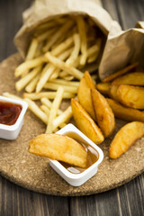 fried potatoes and french fries in paper bags with ketchup and sweet and sour sauce. junk food.