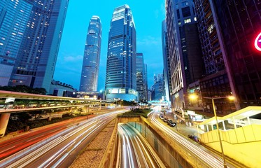 Nightscape of a street corner in Hong Kong with busy traffic trails at rush hour and modern...