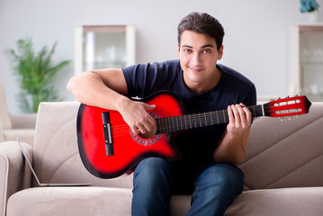 Young man practicing playing guitar at home