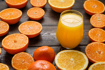 A glass of juice and cut oranges and mandarins on the wooden background