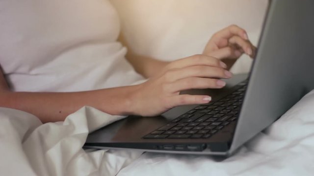 Young woman freelancer working on laptop in bed in hotel room close up