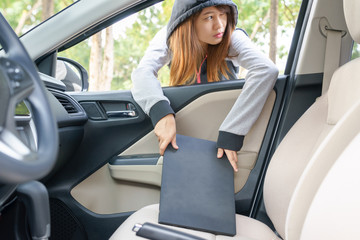 Woman burglar steal a laptop through the window of car - theft concept.