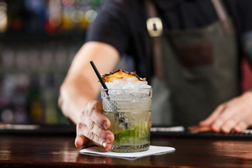 Cheerful bartender gives the cocktail to customer.