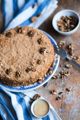 round delicious honey cake in blue white plate on a brown wooden background, bright flour, walnuts with white blue striped tea towel Golden amber honey with a fork