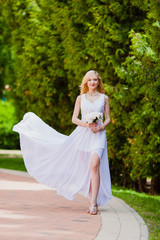 Fototapeta na wymiar Young beautiful bride in white dress is walking in the summer park with a bridal bouquet 