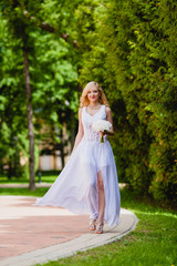 Obraz na płótnie Canvas Young beautiful bride in white dress is walking in the summer park with a bridal bouquet 