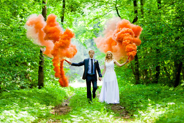 The bride and groom with the orange colored smoke at the background of summer nature