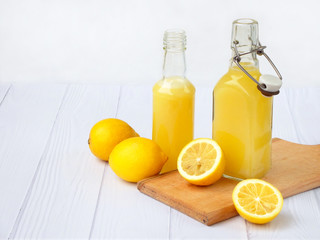 Freshly squeezed lemon juice in bottle and lemons on light background. For vitamin drink or cocktail. Selective focus. Space for text