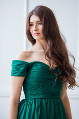 beautiful girl in the emerald green dress brunette with long wavy hair on a white background looking to the side into the distance profile close-up