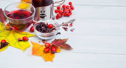 Still life cup of fruit tea and kettle on autumn leaves and vintage wood background.