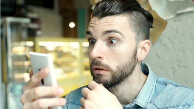 Handsome man with mun bun looks shockes and worried while checking news on smartphone
