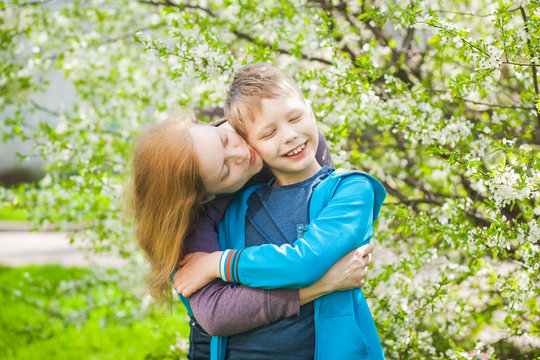 Portrait of happy young caucasian family of mom and cute funny son having fun outdoors in spring blooming garden outdoors. Healthy people in allergy season concept. Horizontal color photography.