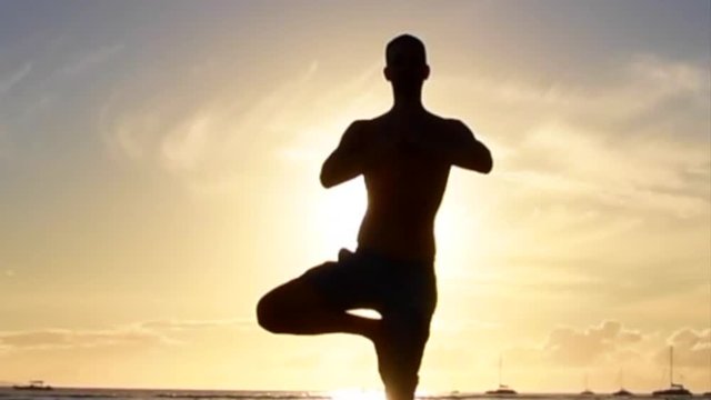 Silhouetted man doing yoga on tropical beach