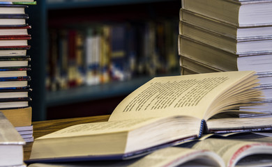 Book in library with old open textbook, stack piles of literature text archive on reading desk, and aisle of bookshelves in school study class room background for academic education learning concept