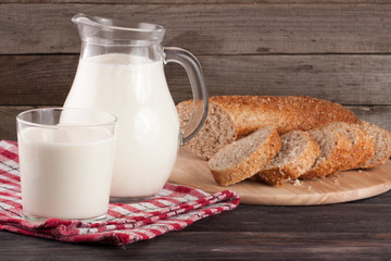 jug and glass of milk with a loaf of bread on a wooden background