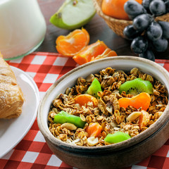 Breakfast made of oatmeal granola, croissants, milk, eggs, coffee and fruits on a red checkered tablecloth. Delicious healthy food.