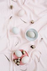 White Easter eggs, quail eggs and feathers on pink textile background. Flat lay, top view. Traditional spring concept. Easter concept.