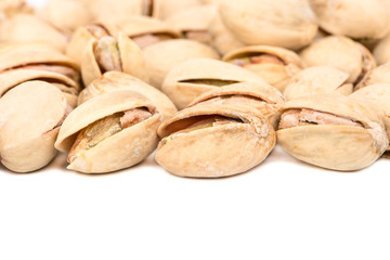 Salted pistachio nuts are scattered on a white background closeup